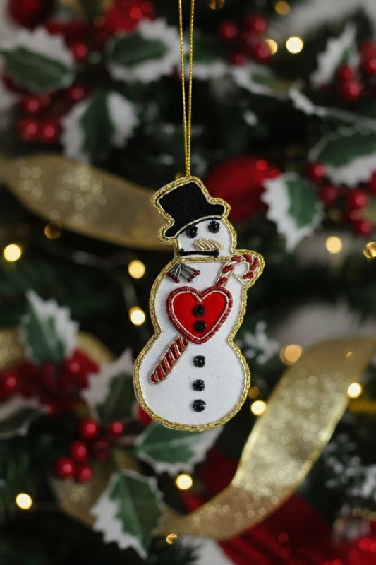 Felt Snowman Ornament — A felt snowman Christmas ornament hanging from a gold string against a blurred decorated Christmas tree with red berries, green holly, and warm string lights. — Zohricanada