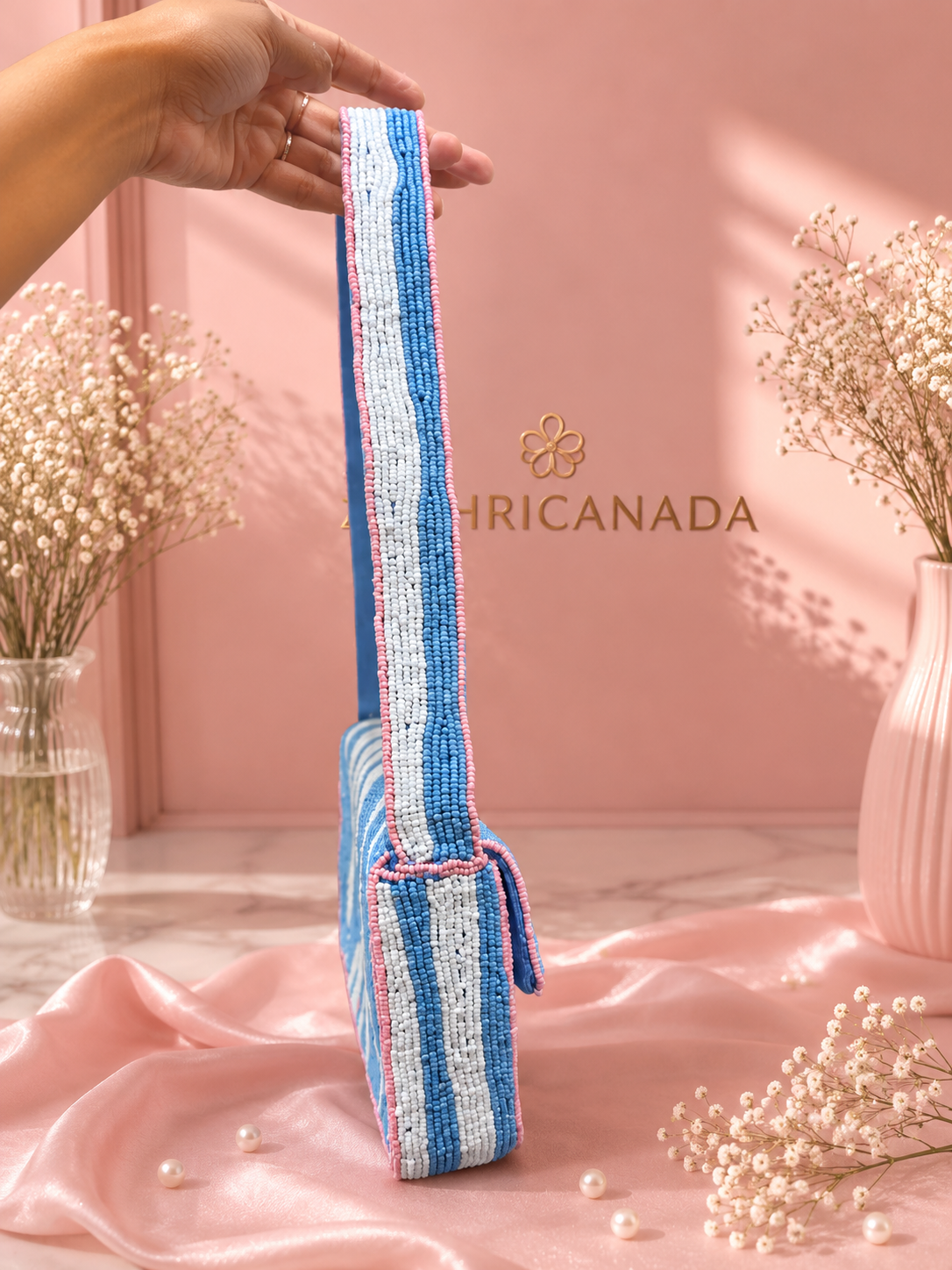Close-up of the woven strap on a blue, white, and pink striped beaded shoulder bag by ZOHRICANADA, shown against a pink backdrop
